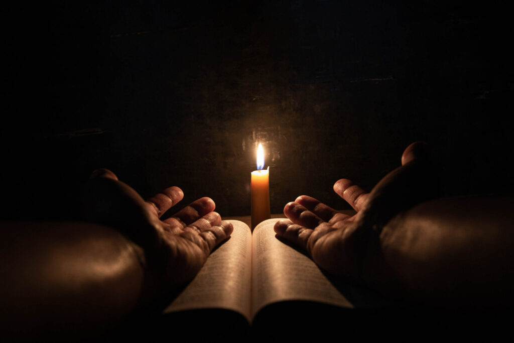 Imagem ilustrativa sobre magia e religião mostrando um fiel orando com uma bíblia e uma vela.