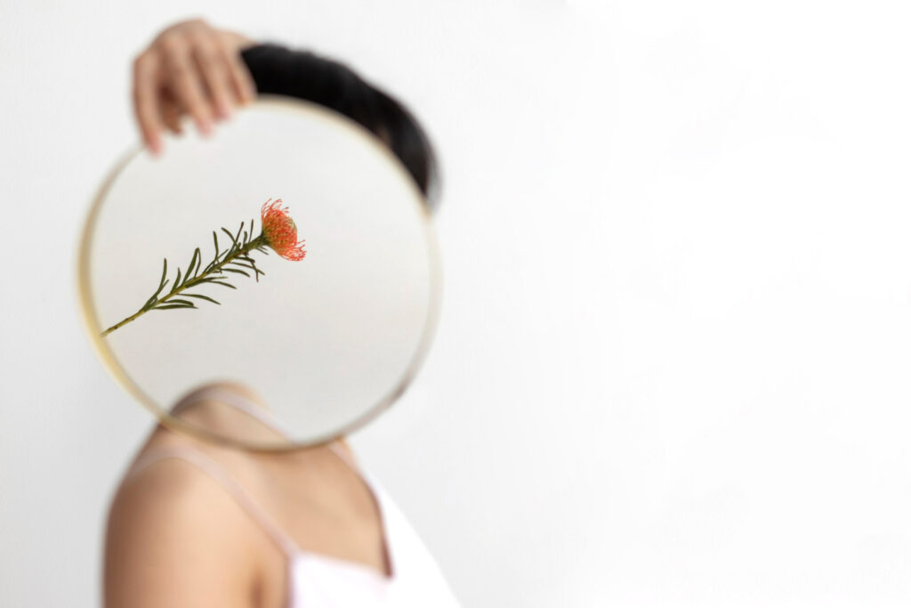 Imagem ilustrando o conteúdo sobre egrégoras mostrando o reflexo de uma flor no espelho, representando a egrégora pessoal da mulher que segura esse espelho.